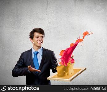 Creativity concept. Handsome businessman holding frame with colorful splashes