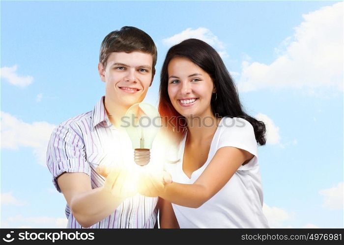 Creativity concept. Young happy couple holding electric bulb in palms
