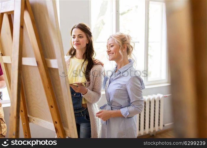 creativity, education and people concept - artists or student girl with palette and teacher discussing painting on easel at art school studio. artists discussing painting on easel at art school