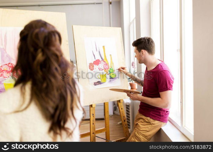 creativity, education and people concept - artists or students with palettes and paint brushes painting still life picture on easels at art school studio. artists painting still life picture at art school