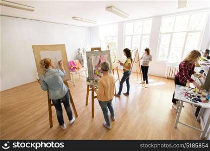 creativity, education and people concept - group of woman artists or students with brushes and palettes painting and drawing still life picture on easels at art school studio. woman artists with brushes painting at art school