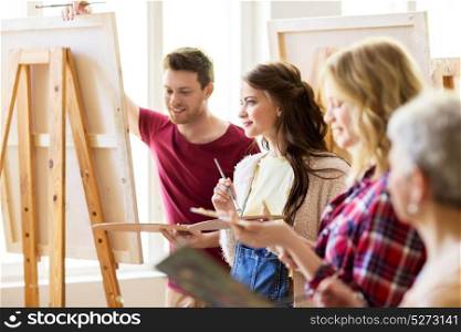 creativity, education and people concept - group of young artists or students with palettes and paint brushes painting on easels at art school studio. group of young artists painting at art school