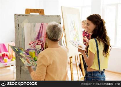 creativity, education and people concept - happy women with brushes and palettes painting still life picture on easel at art school studio. happy women painting at art school studio