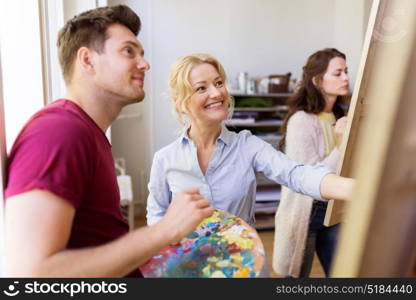 creativity, education and people concept - man artist or student with palette and teacher painting on easel at art school studio. artists with palette and easel at art school