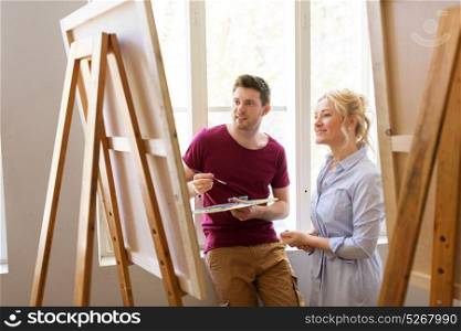 creativity, education and people concept - man artist or student with palette and woman teacher painting on easel at art school studio. artists with palette and easel at art school