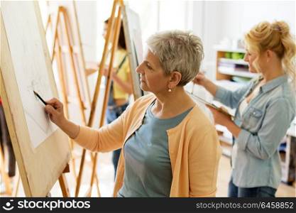 creativity, education and people concept - senior woman drawing on easel at art school studio. senior woman drawing on easel at art school studio