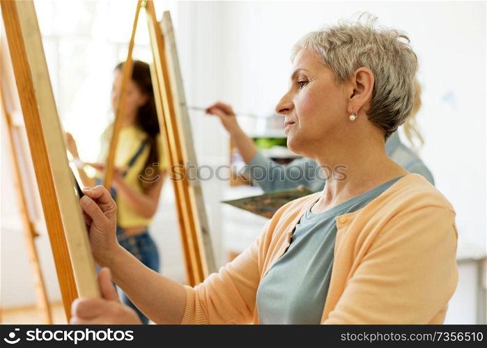 creativity, education and people concept - senior woman drawing on easel at art school studio. senior woman drawing on easel at art school studio
