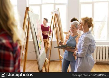 creativity, education and people concept - women artists discussing painting on easel at art school studio. artists discussing painting on easel at art school