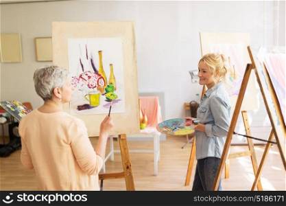 creativity, education and people concept - women artists painting still life picture on easels at art school studio and talking. artist women with easels painting at art school