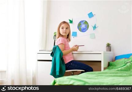 creativity, education, people and childhood concept - pensive little girl doing homework or drawing at home. little girl doing homework or drawing at home