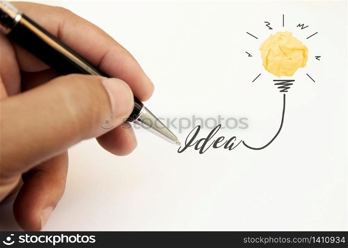 Creativity inspiration, ideas and innovation concepts with lightbulb and paper crumpled ball. Hand of businessman writing text idea with pen.