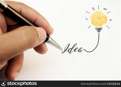 Creativity inspiration, ideas and innovation concepts with lightbulb and paper crumpled ball. Hand of businessman writing text idea with pen.