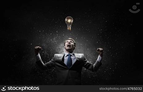 Creativity is my power. Young businessman with hands up screaming at light bulb above his head