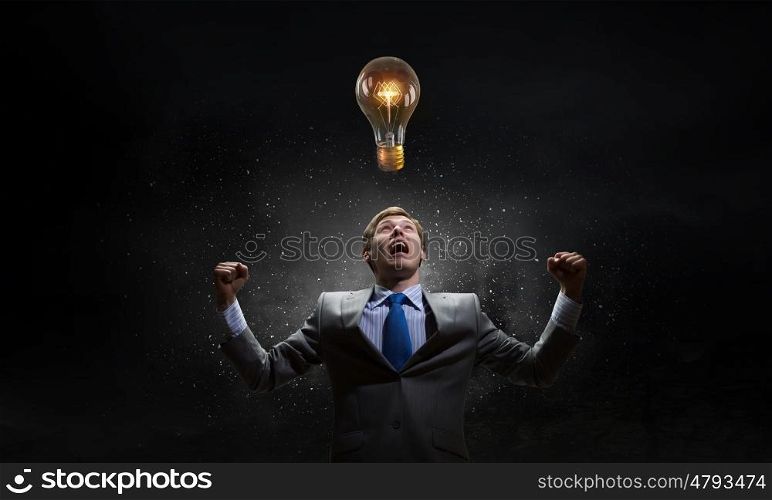Creativity is my power. Young businessman with hands up screaming at light bulb above his head