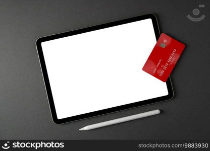 Credit card lying on tablet with blank screen on dark gray table