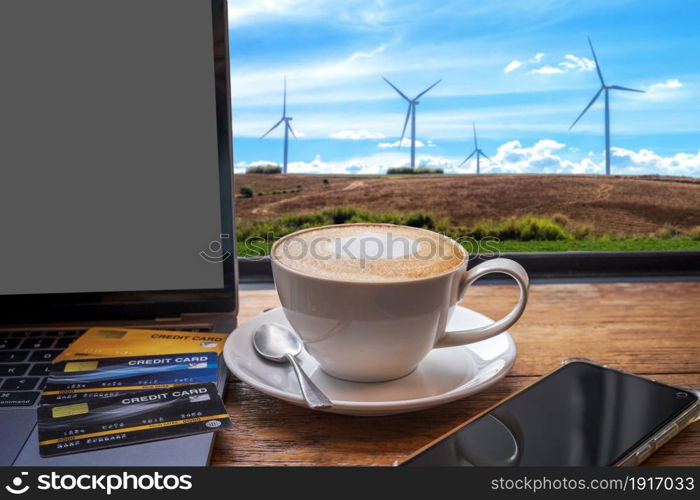 Credit card of laptop computer,smartphone and Hot coffee latte with latte art milk foam in cup mug on with wind turbines against and blue sky background,Online banking Concept