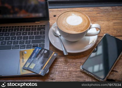 Credit card of laptop computer,smartphone and Hot coffee latte with latte art milk foam in cup mug on wooden background,Online banking Concept