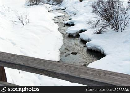 Creek running through snow covered banks and wooden rail of a bridge