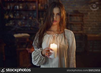 Creepy demonic woman holds candle, demons casting out. Exorcism, mystery paranormal ritual, dark religion, night horror, potions on shelf on background. Creepy woman holds candle, demons casting out