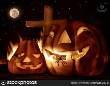 Creepy Halloween night, glowing carved pumpkin with scary horrible spiders, cross and burning flame on the graveyard in full moon night