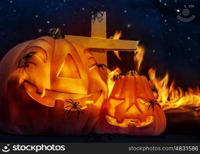 Creepy Halloween night, glowing carved pumpkin with scary horrible spiders, cross and burning flame on the graveyard in mysterious dark night