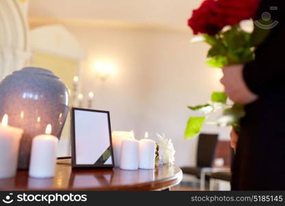 cremation, people and mourning concept - cinerary urn, photo frame with black ribbon and woman holding red roses at funeral in church. cremation urn and woman at funeral in church