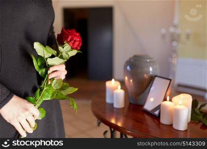 cremation, people and mourning concept - woman with red roses and cinerary urn at funeral in church. woman with cremation urn at funeral in church