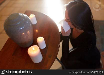 cremation, people and mourning concept - woman with wipe and cinerary urn crying at funeral in church. woman with cremation urn at funeral in church
