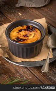 Creme brulee. Bowls with French vanilla cream dessert with caramelised sugar on top, spoons, dark rustic table. Leite creme, portuguese desert similar to creme brulee, cream brulee and burnt cream.