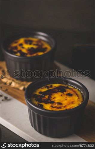 Creme brulee. Bowls with French vanilla cream dessert with caramelised sugar on top, spoons, dark rustic table.