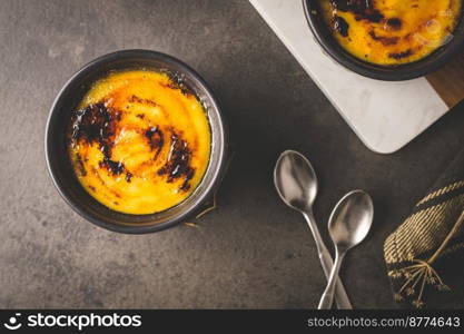 Creme brulee. Bowls with French vanilla cream dessert with caramelised sugar on top, spoons, dark rustic table.