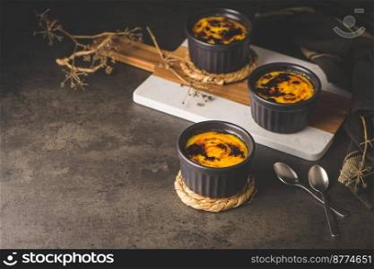 Creme brulee. Bowls with French vanilla cream dessert with caramelised sugar on top, spoons, dark rustic table.