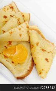 Crepe on a plate with mandarin. It is isolated on a white background. A detailed photo fried thin pancake.