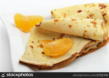 Crepe on a plate with mandarin. It is isolated on a white background. A detailed photo fried thin pancake.