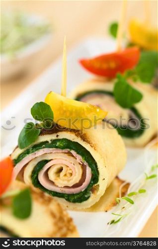 Crepe rolls as finger food filled with spinach and ham garnished with cherry tomato and watercress (Selective Focus, Focus on the right upper part of the crepe roll)