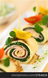 Crepe rolls as finger food filled with spinach and ham garnished with cherry tomato and watercress (Selective Focus, Focus on the right upper part of the crepe roll)