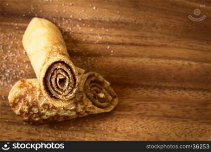 Crepe rolls filled with cinnamon and sugar, photographed overhead on wood with natural light (Selective Focus, Focus on the front of the upper roll)