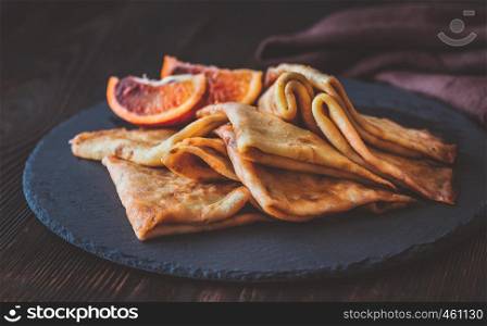 Crepes Suzette with slices of blood orange on the black stone board