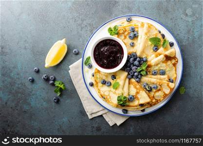 Crepes, thin pancakes with blueberry jam and fresh berries with lemon zest