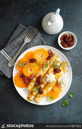 Crepes, thin pancakes with fresh tangerine slices, pecan nuts, syrup and whipped cream