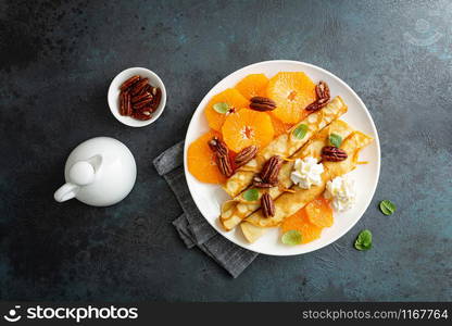 Crepes, thin pancakes with fresh tangerine slices, pecan nuts, syrup and whipped cream