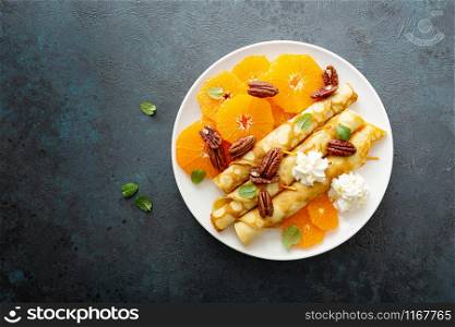 Crepes, thin pancakes with fresh tangerine slices, pecan nuts, syrup and whipped cream
