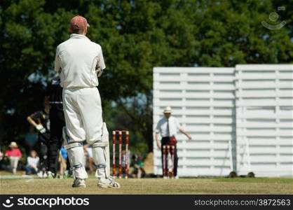 cricketers on an english village green playing a match on a hot summers day