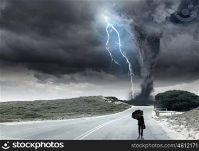 Crisis concept. Back view of businessman with umbrella and suitcase facing tornado