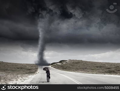 Crisis concept. Back view of businessman with umbrella and suitcase facing tornado