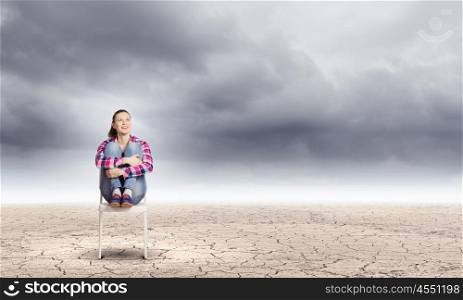 Crisis concept. Young woman sitting in chair among desert