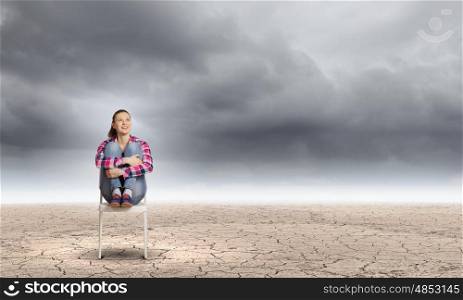 Crisis concept. Young woman sitting in chair among desert