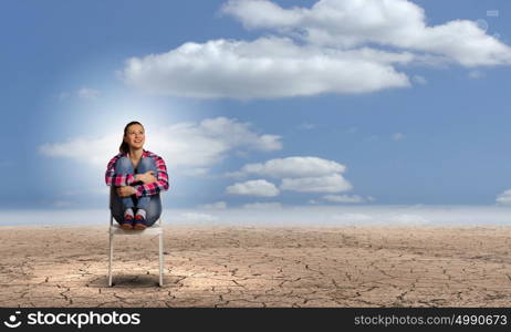 Crisis concept. Young woman sitting in chair among desert