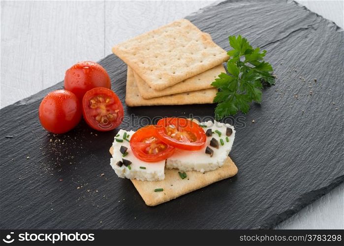 Crispbread with fromage, tomato and olives on black ardoise tray.