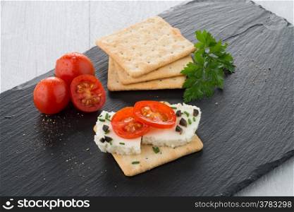 Crispbread with fromage, tomato and olives on black ardoise tray.